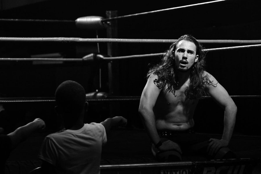 Long-haired wrestler resting on the ropes in a ring, black and white